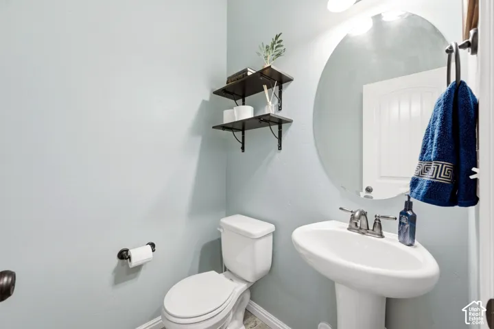 Pedestal sink with a chrome two-handle faucet, circular mirror, and wall-mounted shelving