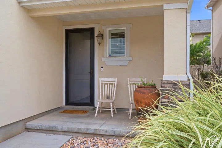 Covered front porch featuring stucco exterior, a decorative wall-mounted light fixture, and a window with blinds