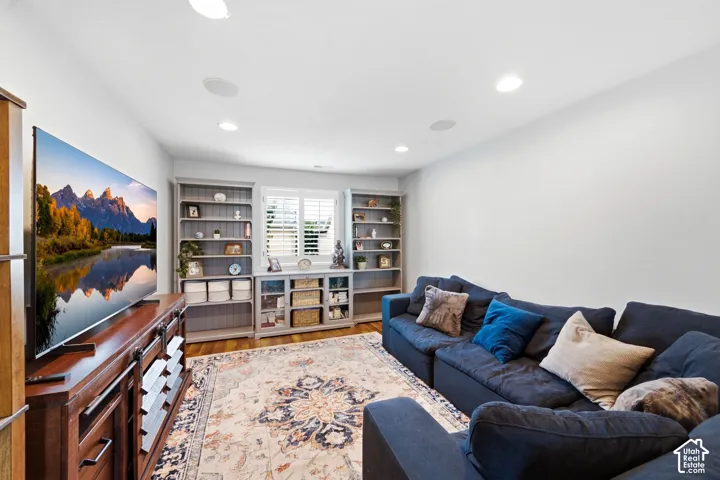 Recessed lighting with integrated sound system, wood-finish flooring, custom built-in shelving, window with plantation shutters, and a wood media console