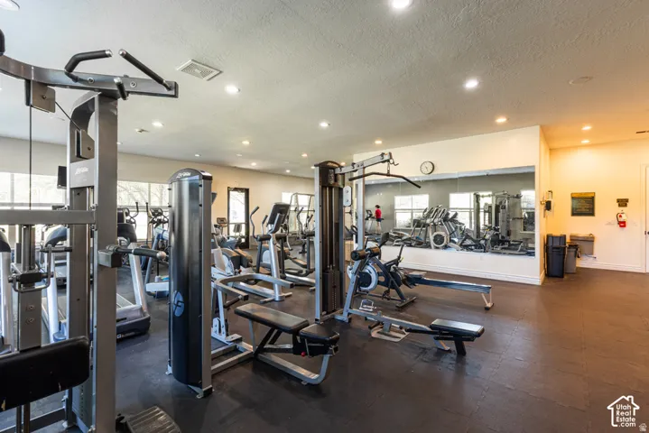 Fitness center with a variety of exercise equipment, mirrored wall, recessed lighting, and large windows