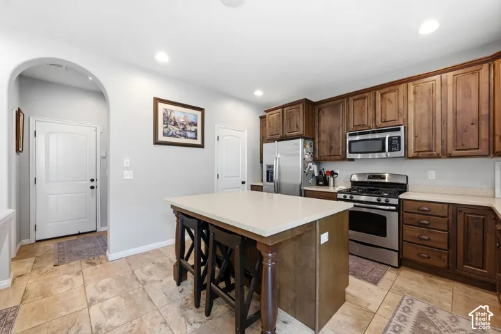 Kitchen featuring a central island with countertop, wood-finish cabinetry, stainless steel appliances, and tile flooring