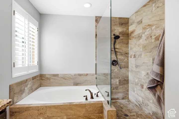 Walk-in shower with natural stone tile surround, glass enclosure, and a built-in tub