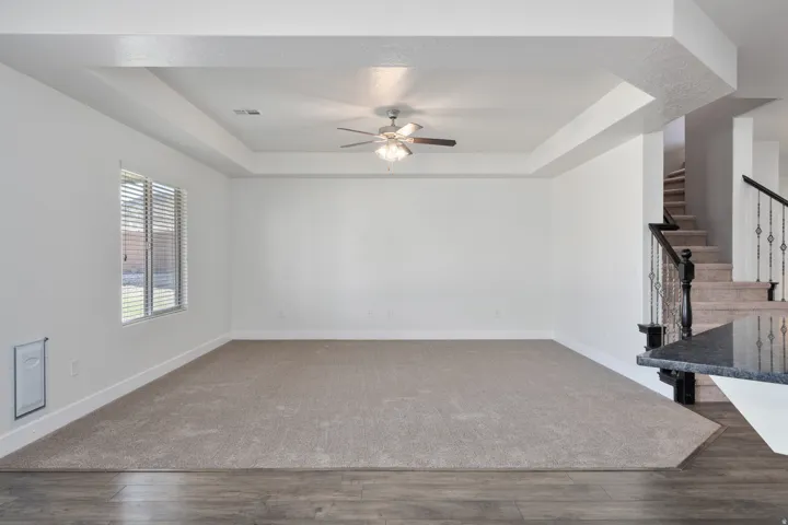 Recessed ceiling with a central fan, light-toned carpet, wood-finish flooring, and a staircase with wrought iron balusters