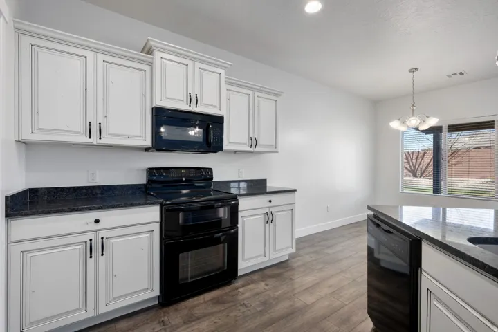 White shaker-style cabinetry with dark hardware, dark countertops, black electric range with double oven, built-in microwave, and wood-finish flooring