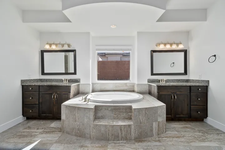 Soaking tub with tiled surround, dual vanities with granite countertops, and decorative wall mirrors