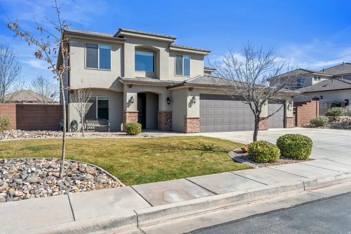 Two-story stucco exterior with stone accents, covered entry, attached three-car garage, and a manicured lawn
