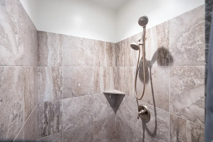 Tiled shower with a corner shelf and a brushed nickel dual shower head
