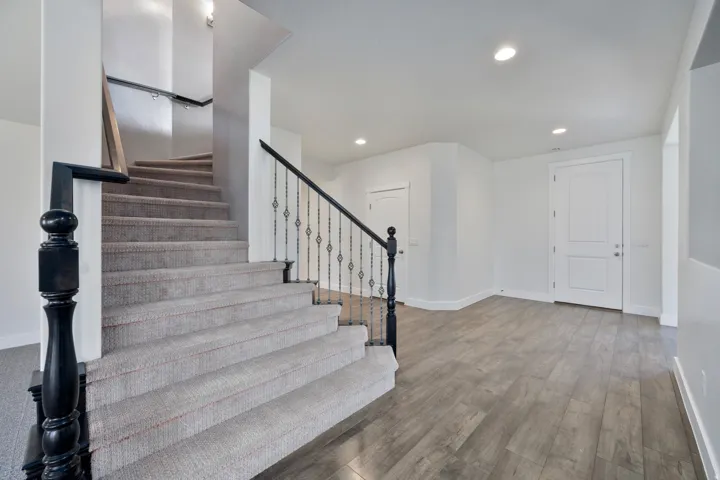 Carpeted staircase with black newel post and wrought iron balusters
