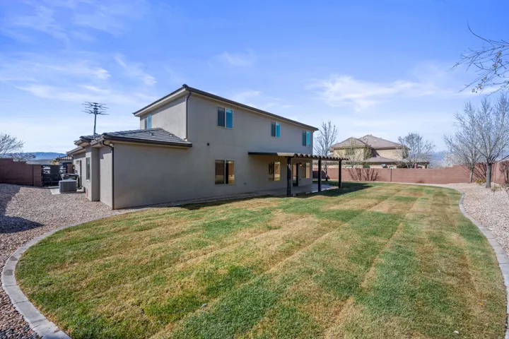 Expansive backyard featuring a manicured lawn, gravel border, and a covered patio with a pergola