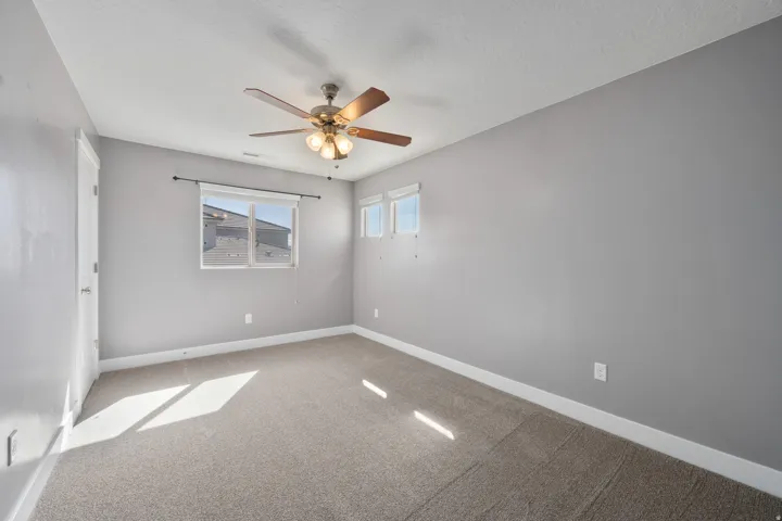 Carpeted room with a ceiling fan, multiple windows, and a white door