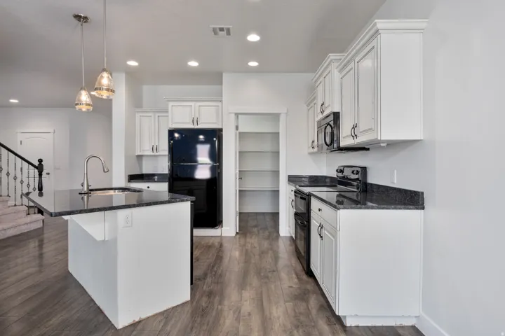 Kitchen featuring an island with sink, dark countertops, white cabinetry, and wood-finish flooring