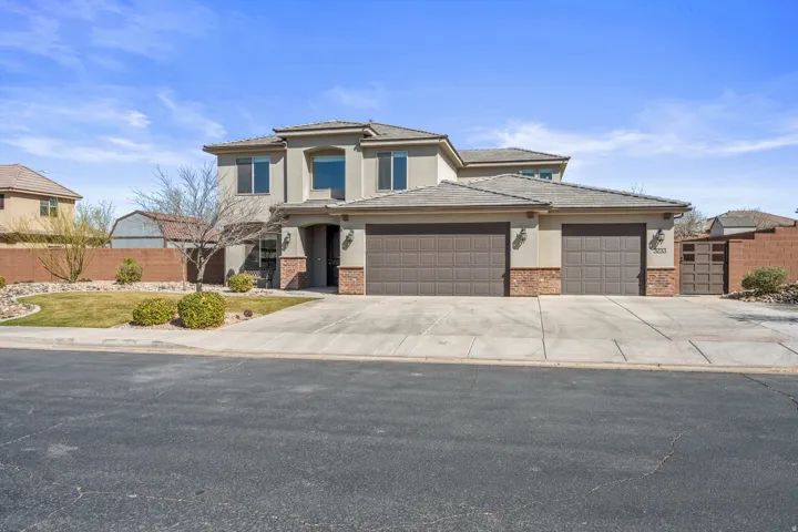 Stucco exterior with brick accents, multi-car garage, concrete driveway, and a landscaped front yard