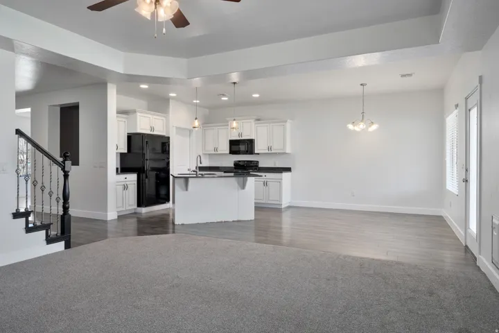 Tray ceiling with a ceiling fan, wood-finish flooring, white cabinetry, black appliances, and a wrought iron staircase