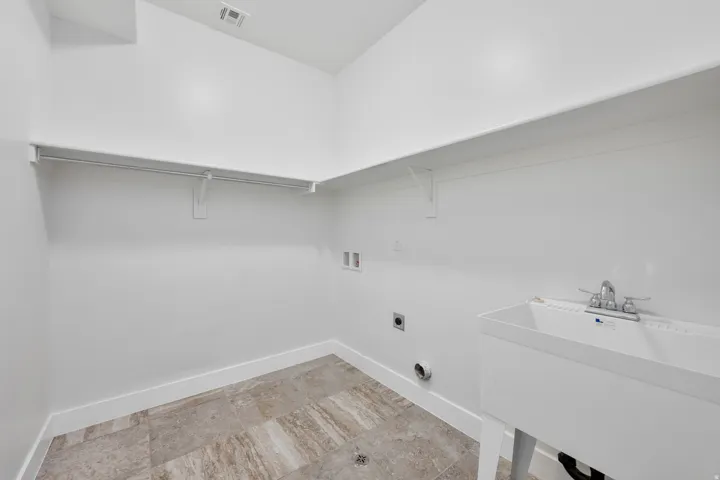 Laundry area featuring tiled flooring, a utility sink with a chrome faucet, and integrated shelving with a hanging rod