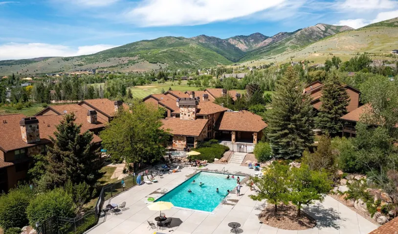 Expansive outdoor swimming pool with surrounding concrete patio, mature landscaping, and mountain backdrop