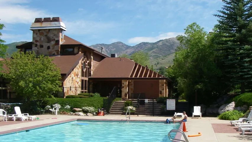 Spacious swimming pool with surrounding concrete decking, complemented by a stone and wood-sided building featuring a prominent stone tower