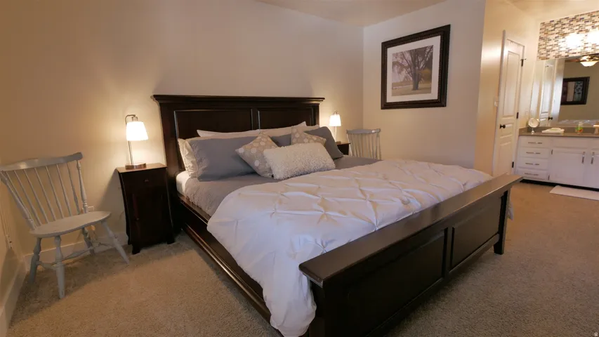 Carpeted bedroom with a dark wood bed frame, recessed lighting, and a white vanity with a mirror and overhead light fixture