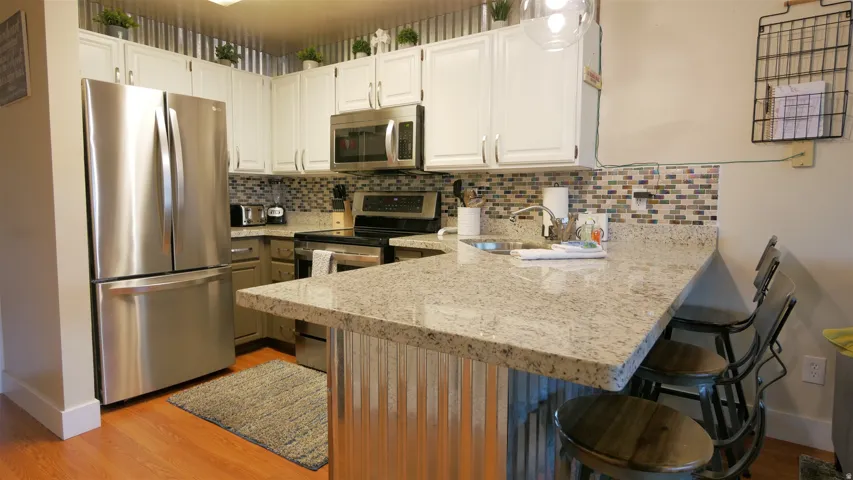 Stainless steel appliances, white cabinetry, a tiled backsplash, and a breakfast bar with a stone-finish countertop