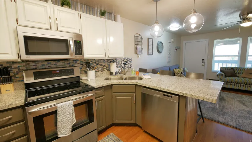Stainless steel appliances, granite countertops, tile backsplash, wood-finish flooring, and white cabinetry