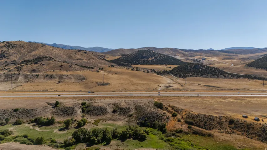 Expansive natural landscape featuring rolling hills, a prominent highway, and distant mountain ranges