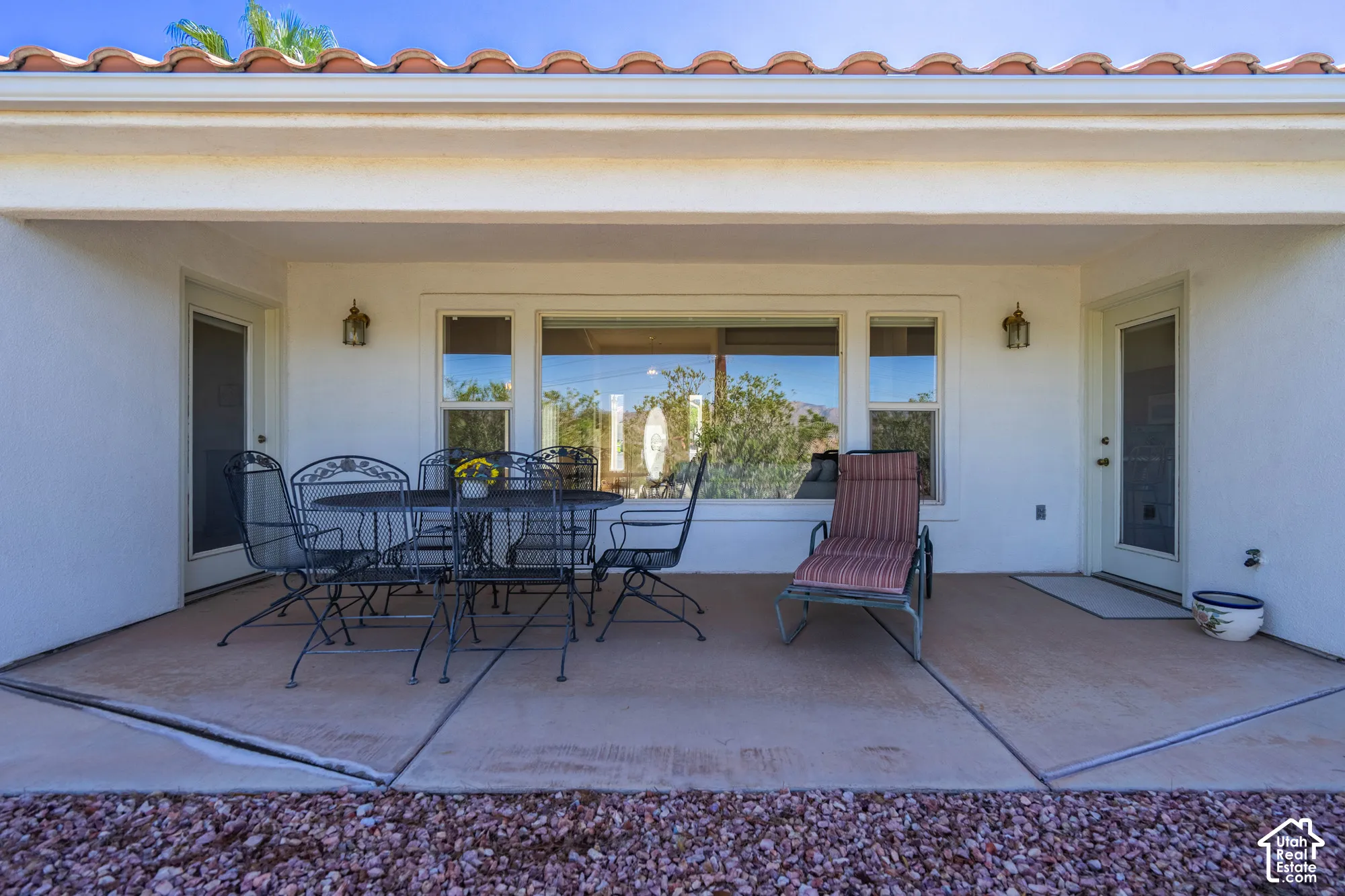Covered concrete patio with two exterior doors, multiple windows, and exterior wall sconces