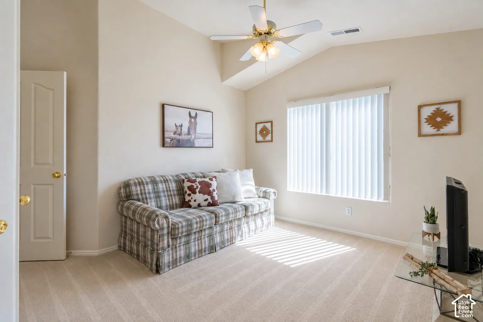 Vaulted ceiling, ceiling fan with integrated lighting, natural light from a large window, vertical blinds, and neutral-toned carpeting