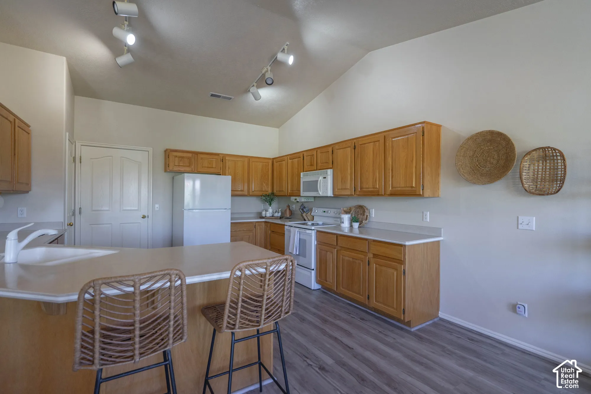 Kitchen featuring vaulted ceilings, wood-finish cabinetry, a peninsula with a built-in sink, integrated appliances, and wood-finish flooring
