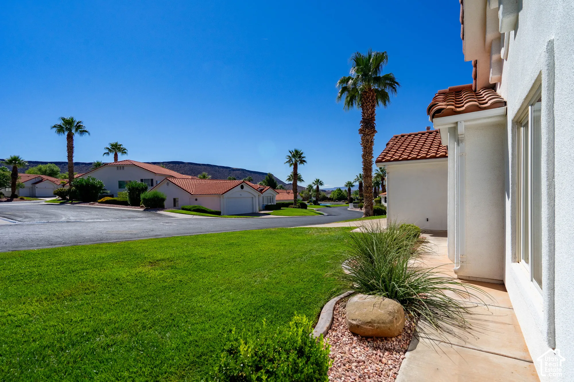 Stucco exterior with a terracotta tile roof, complemented by a manicured lawn and mature palm trees