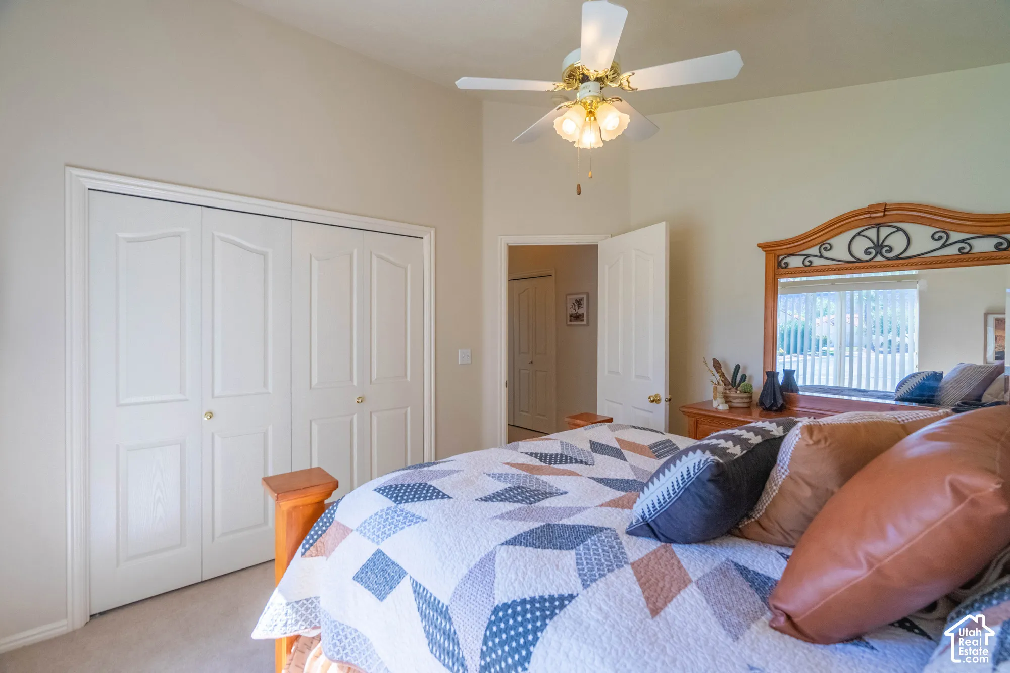 Vaulted ceiling, ceiling fan with integrated lighting, dual bi-fold closet doors, wall mirror with decorative frame, light-toned carpeting