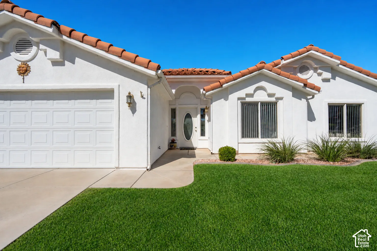 Stucco exterior with terracotta tile roofing, a concrete driveway, and a manicured lawnPhoto of lawn is altered to be more green.