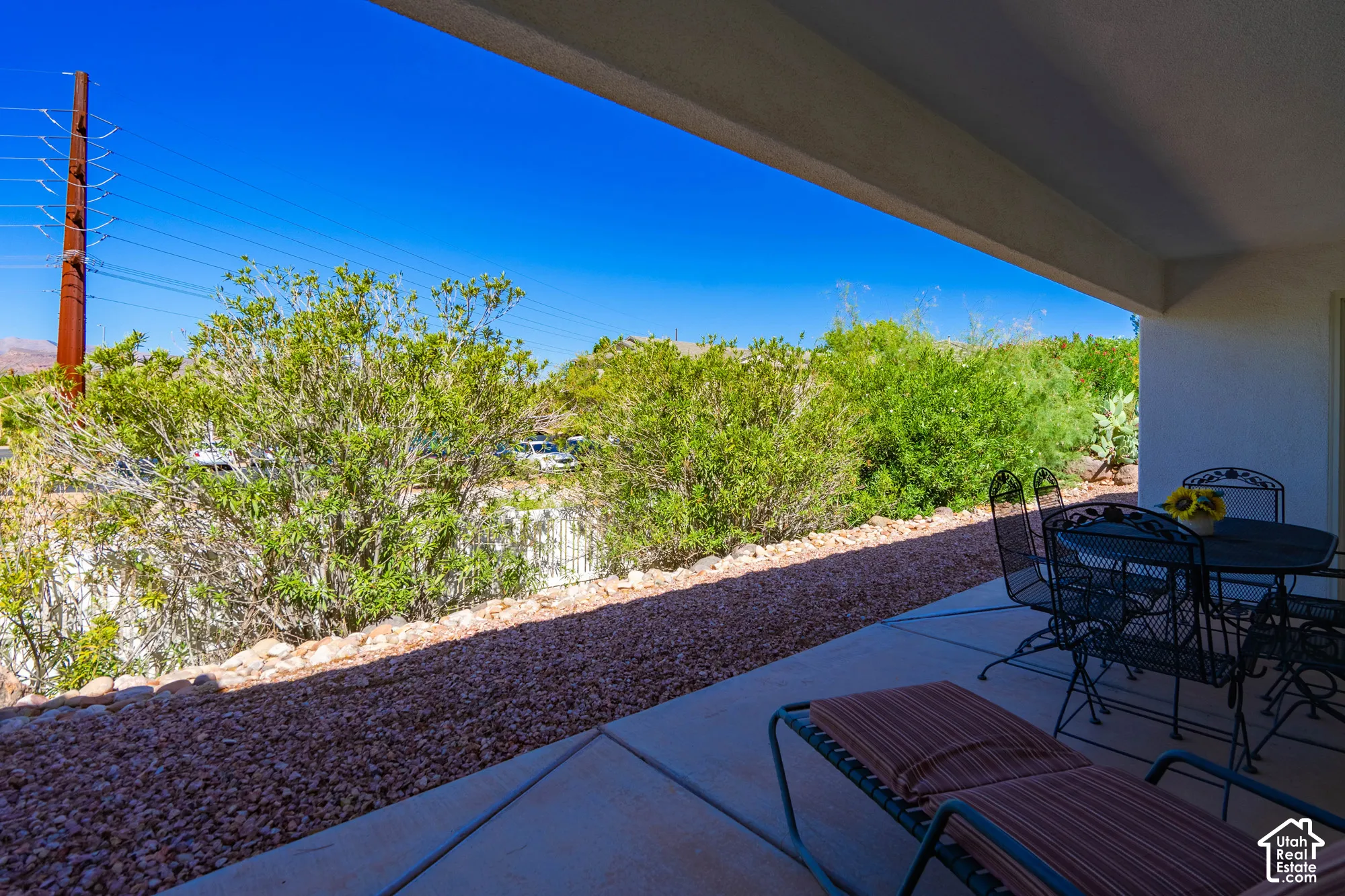 Covered patio with concrete flooring, gravel landscaping, and mature shrubbery