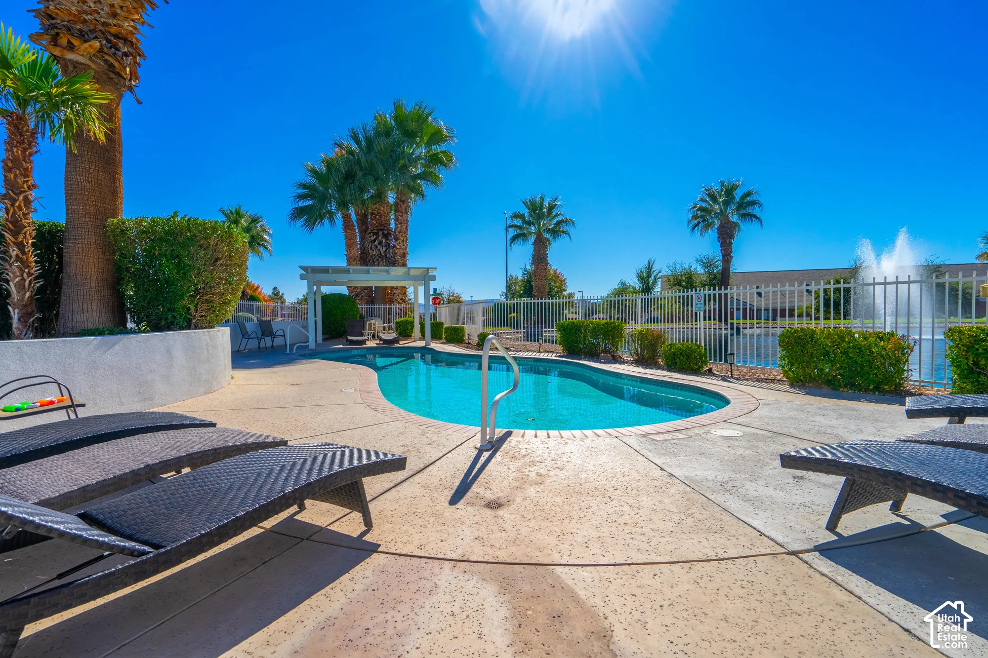 Curved swimming pool with perimeter decking, white metal fencing, and mature palm trees