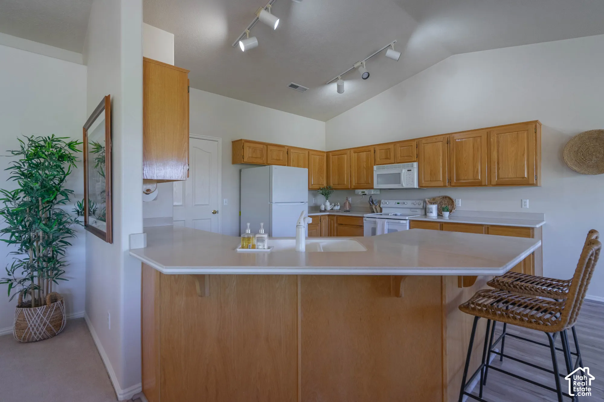 Kitchen featuring wood cabinetry, light-toned countertops, white appliances, and track lighting