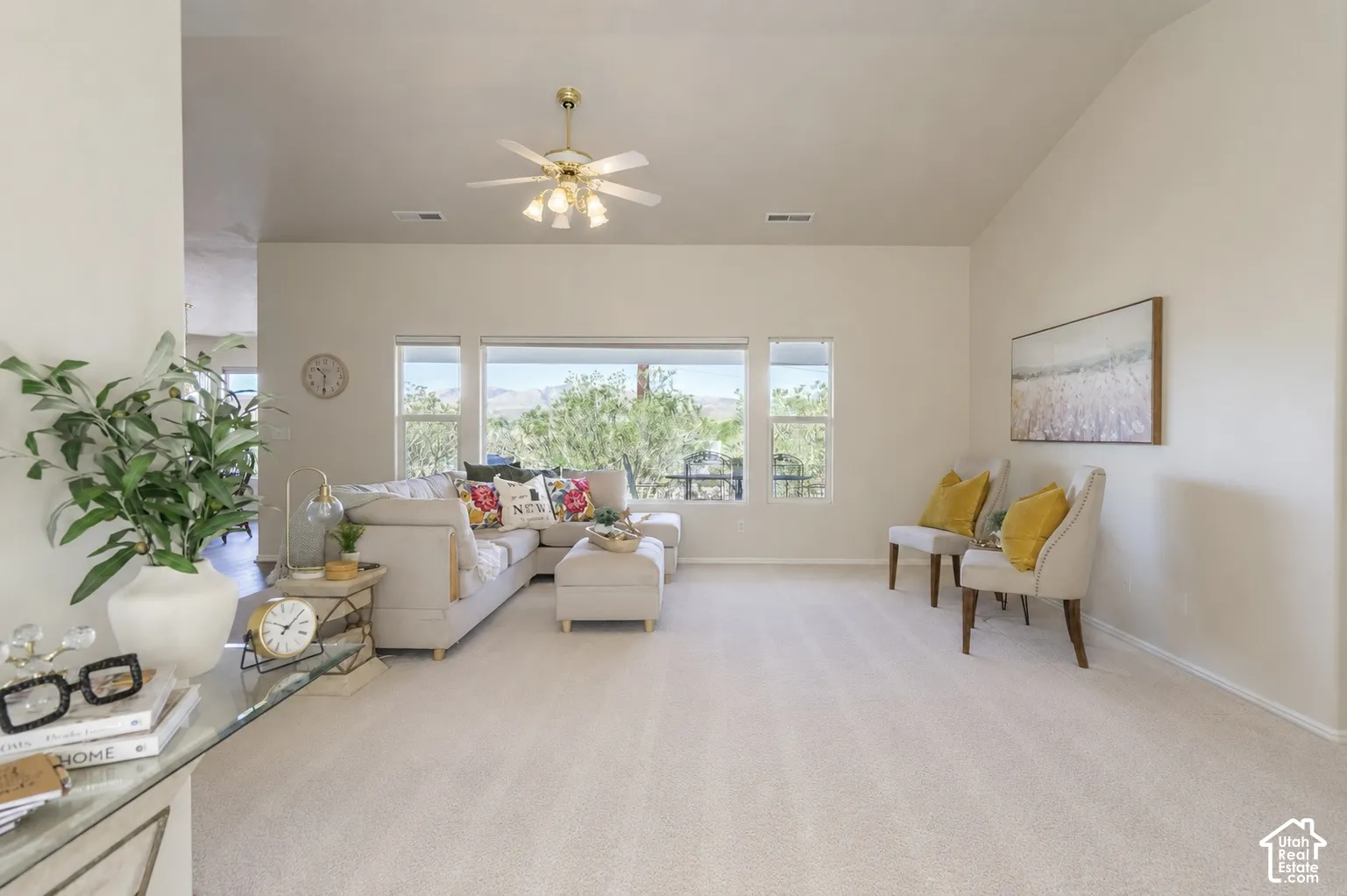 Bright, open living space featuring expansive windows with natural light, light wood-finish flooring throughout, ceiling fan with integrated lighting, and neutral wall finishes
