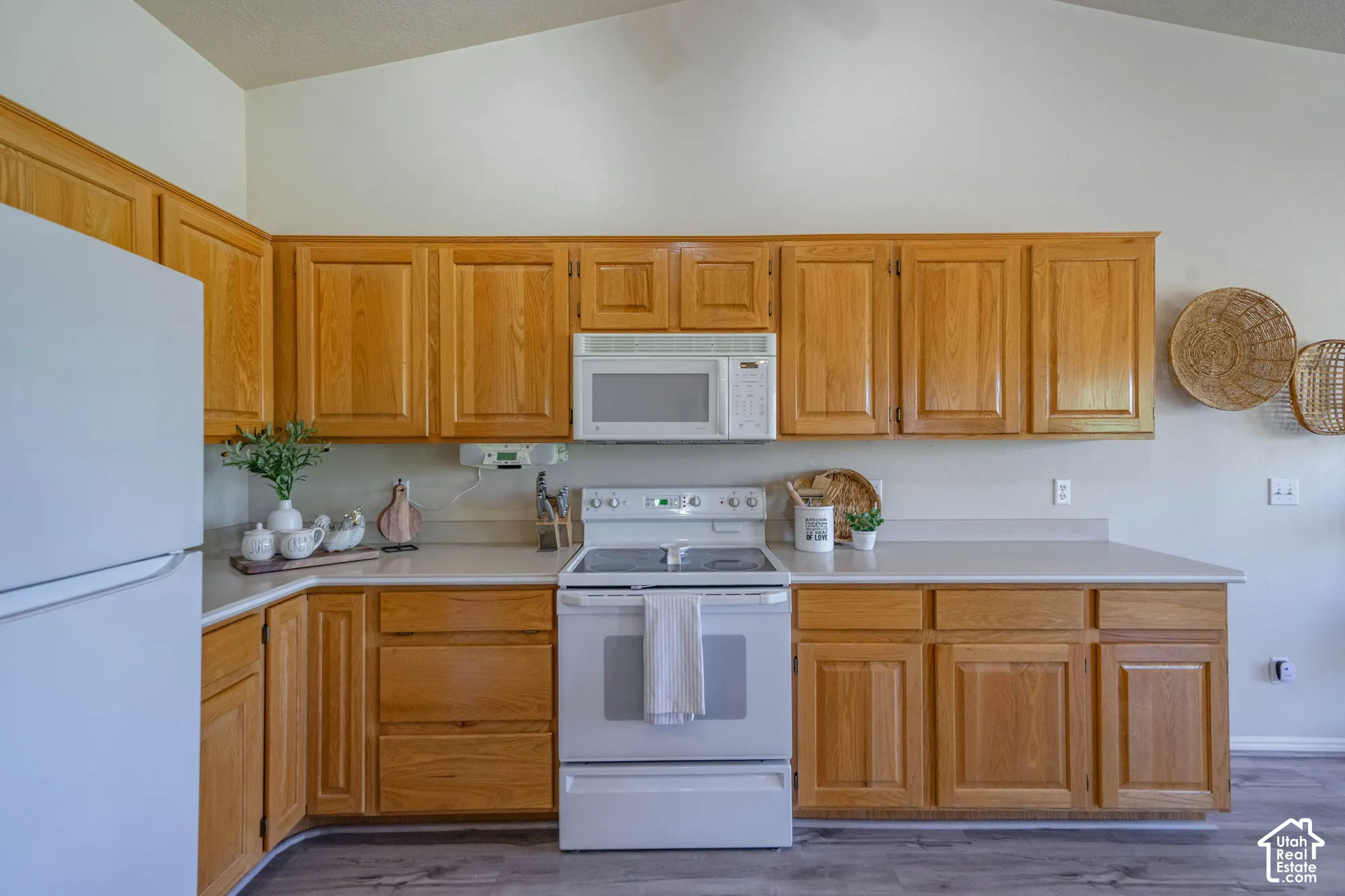 Vaulted ceiling, wood-finish cabinetry, white countertops, built-in microwave, and electric range