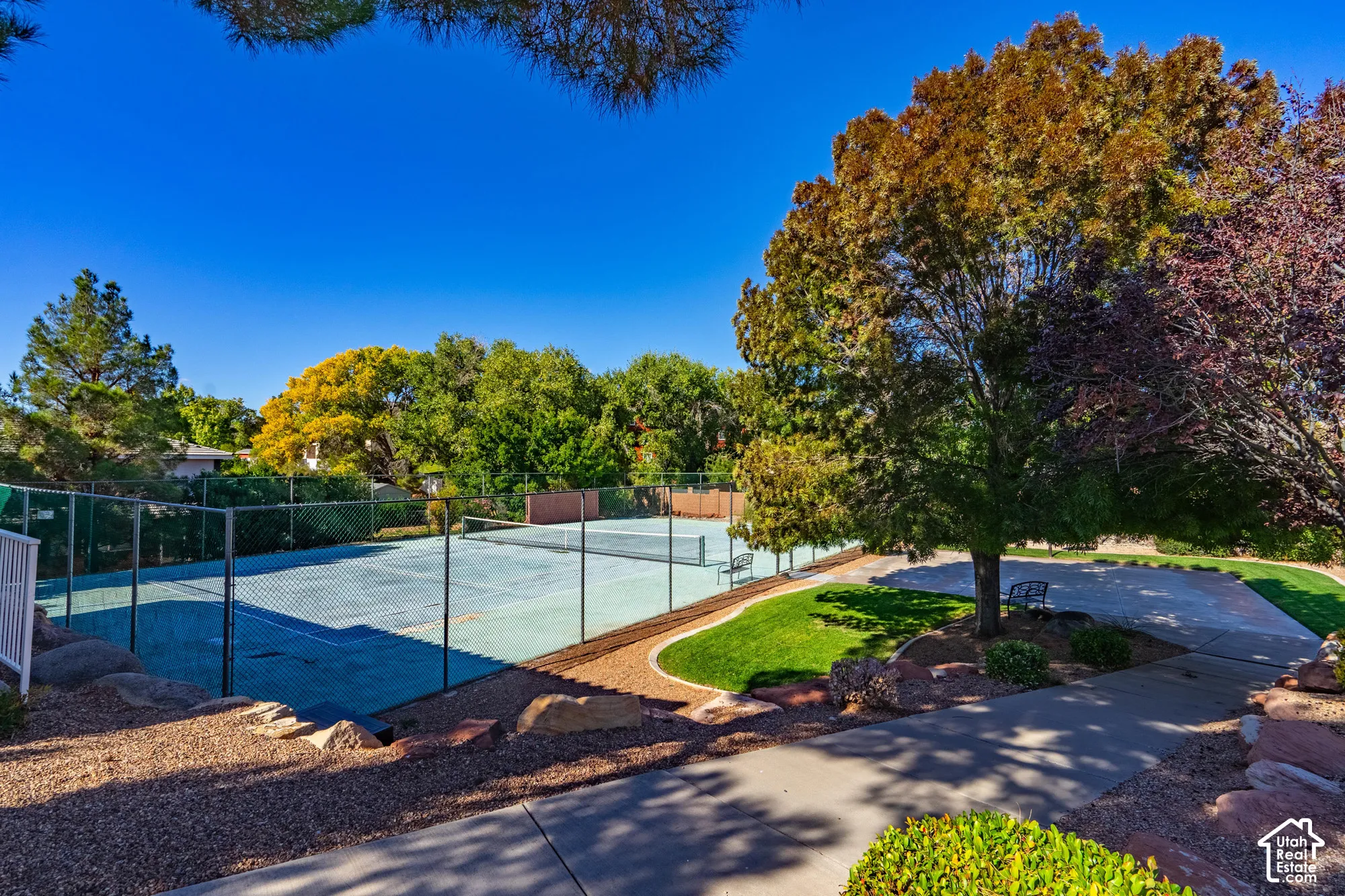 Tennis court with perimeter fencing, surrounded by mature trees and landscaping