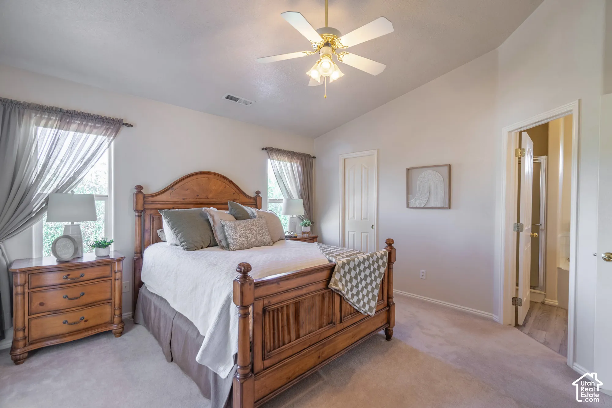 Vaulted ceiling with an attached ceiling fan, two windows with curtain rods, light-toned wall paint, and light-toned carpet flooring