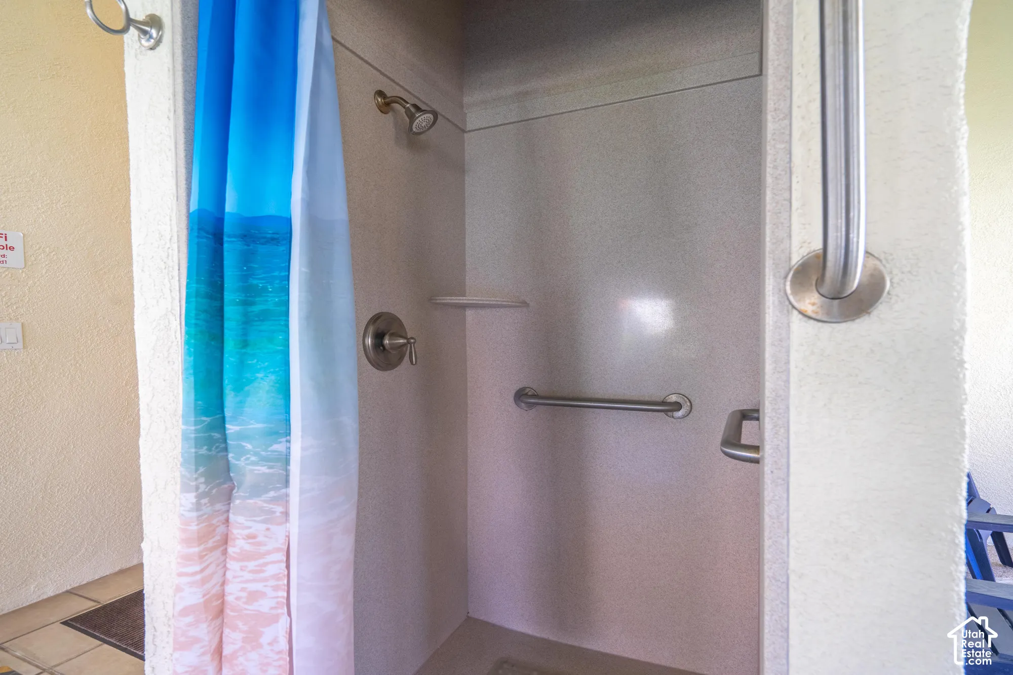 Shower stall with brushed nickel fixtures, a built-in shelf, and grab bars