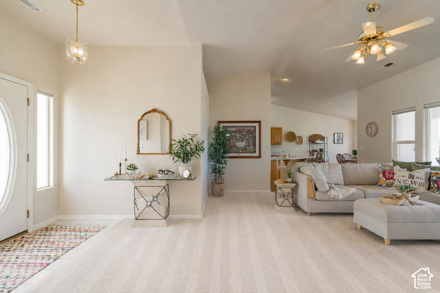 Vaulted ceilings, a decorative entryway light fixture, and abundant natural light illuminate this open-concept living area with plush carpeting
