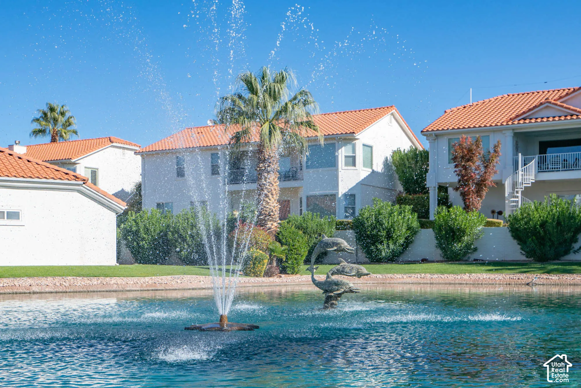 Waterfront property featuring a decorative fountain in the lagoon, mature palm trees, and lush landscaping