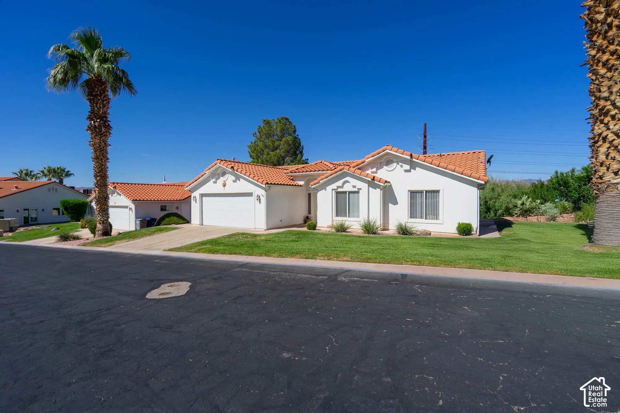 White stucco exterior featuring a terracotta tile roof, attached two-car garage, and a lush green lawn
