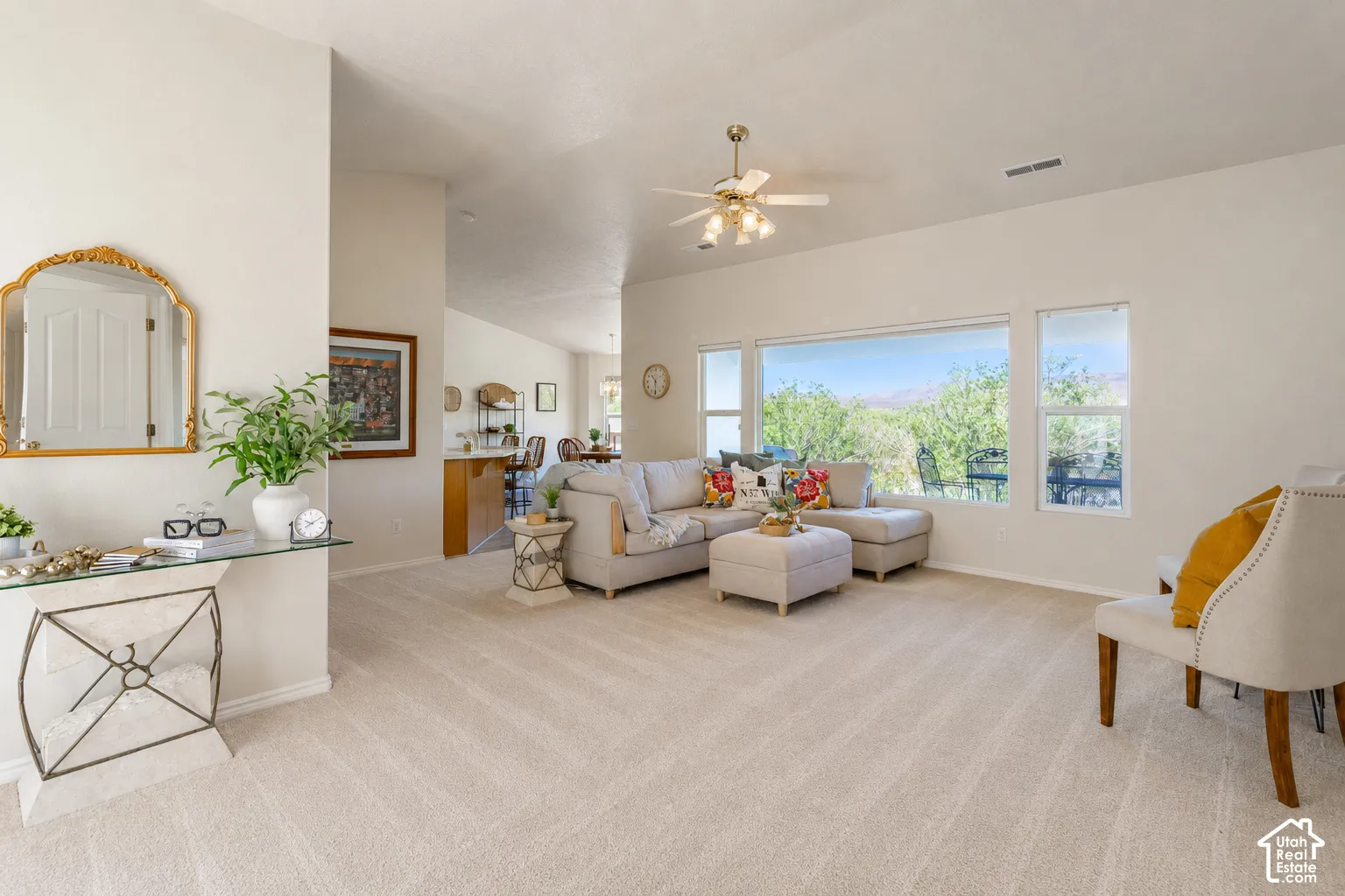 Expansive living area with neutral carpeting, vaulted ceilings, a ceiling fan, and large windows providing ample natural light