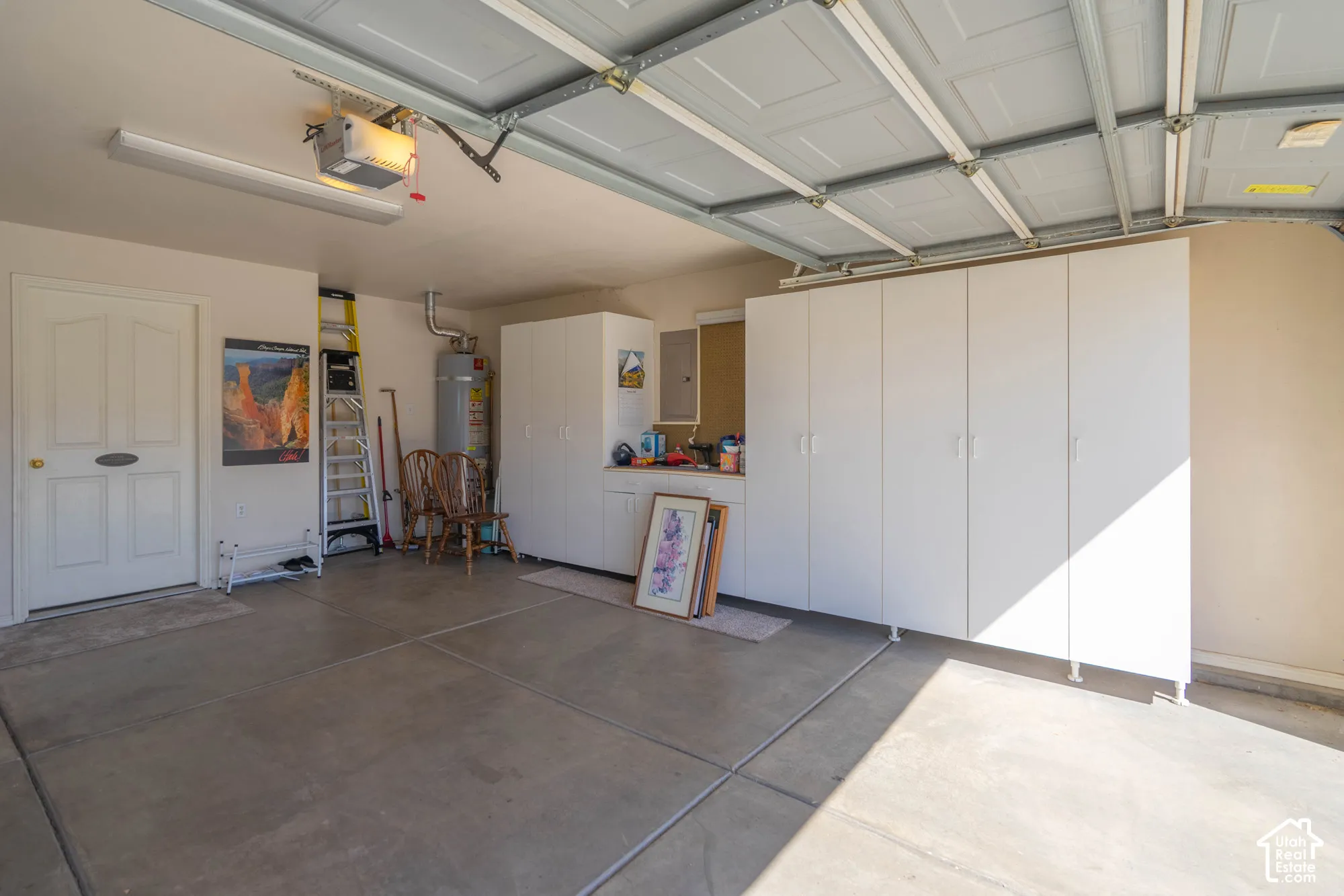 Concrete flooring, built-in white cabinetry, overhead fluorescent lighting, garage door opener, and a water heater
