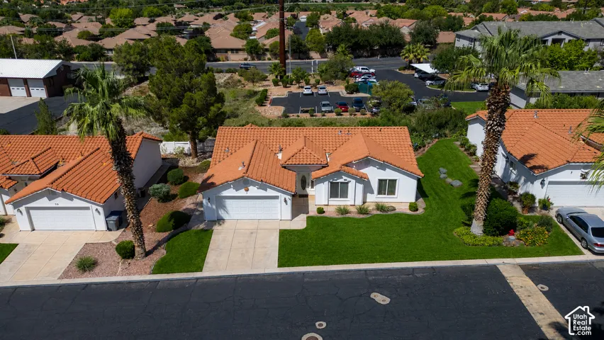 Mediterranean-style residence featuring a terracotta tile roof, attached garage, concrete driveway, and a front lawn with mature palm treesPhoto of lawn is altered to be more green.