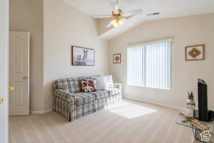 Vaulted ceiling, ceiling fan with integrated lighting, natural light from a large window, vertical blinds, and neutral-toned carpeting