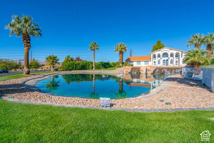 Expansive grassy lawn with a large pond featuring a stone and gravel border, surrounded by mature palm trees