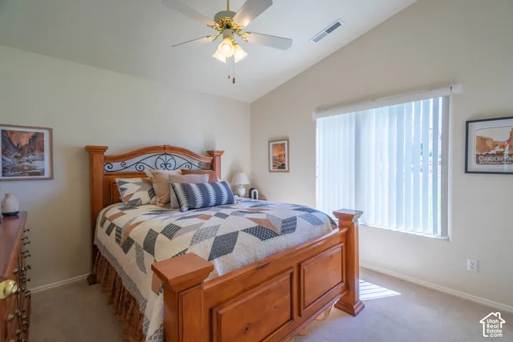 Vaulted ceiling, ceiling fan with integrated lighting, large window with vertical blinds, neutral wall paint, and carpet flooring