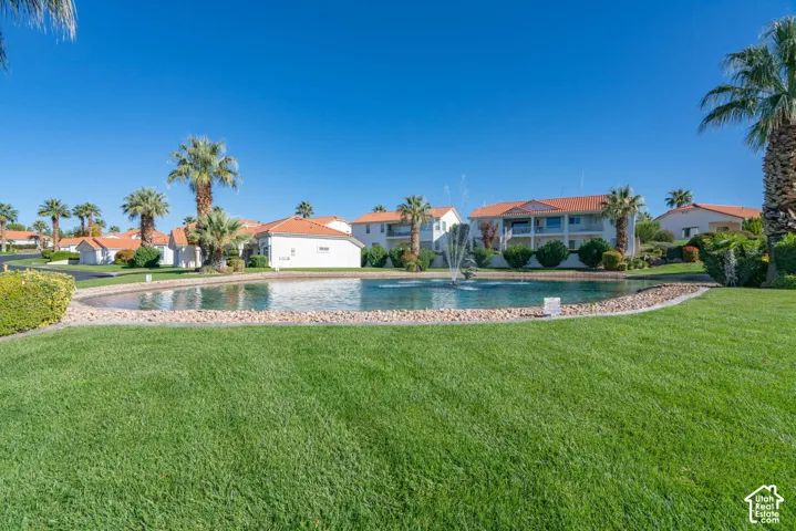 Manicured lawn with a water feature, surrounded by palm trees and low-rise residences featuring red tile roofs
