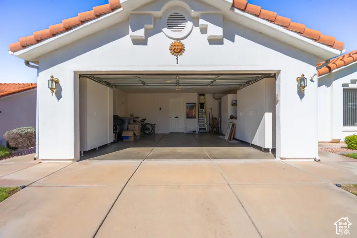 Attached two-car garage with a concrete driveway, stucco exterior, and terracotta-style roof tiles