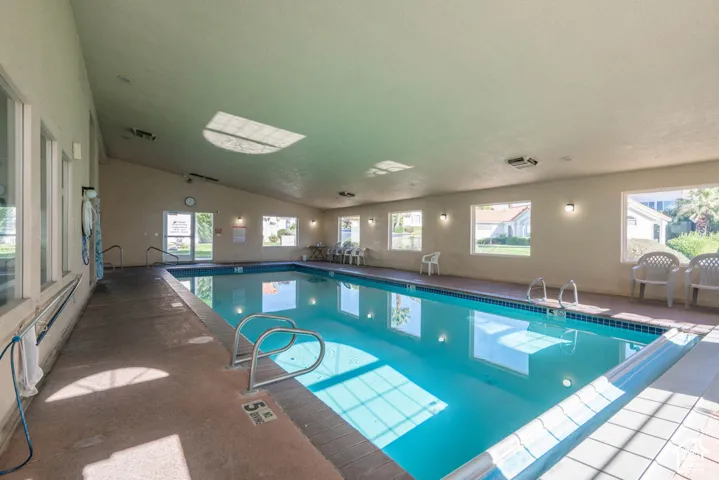 Indoor swimming pool with an angled ceiling, multiple windows, and a concrete pool deck